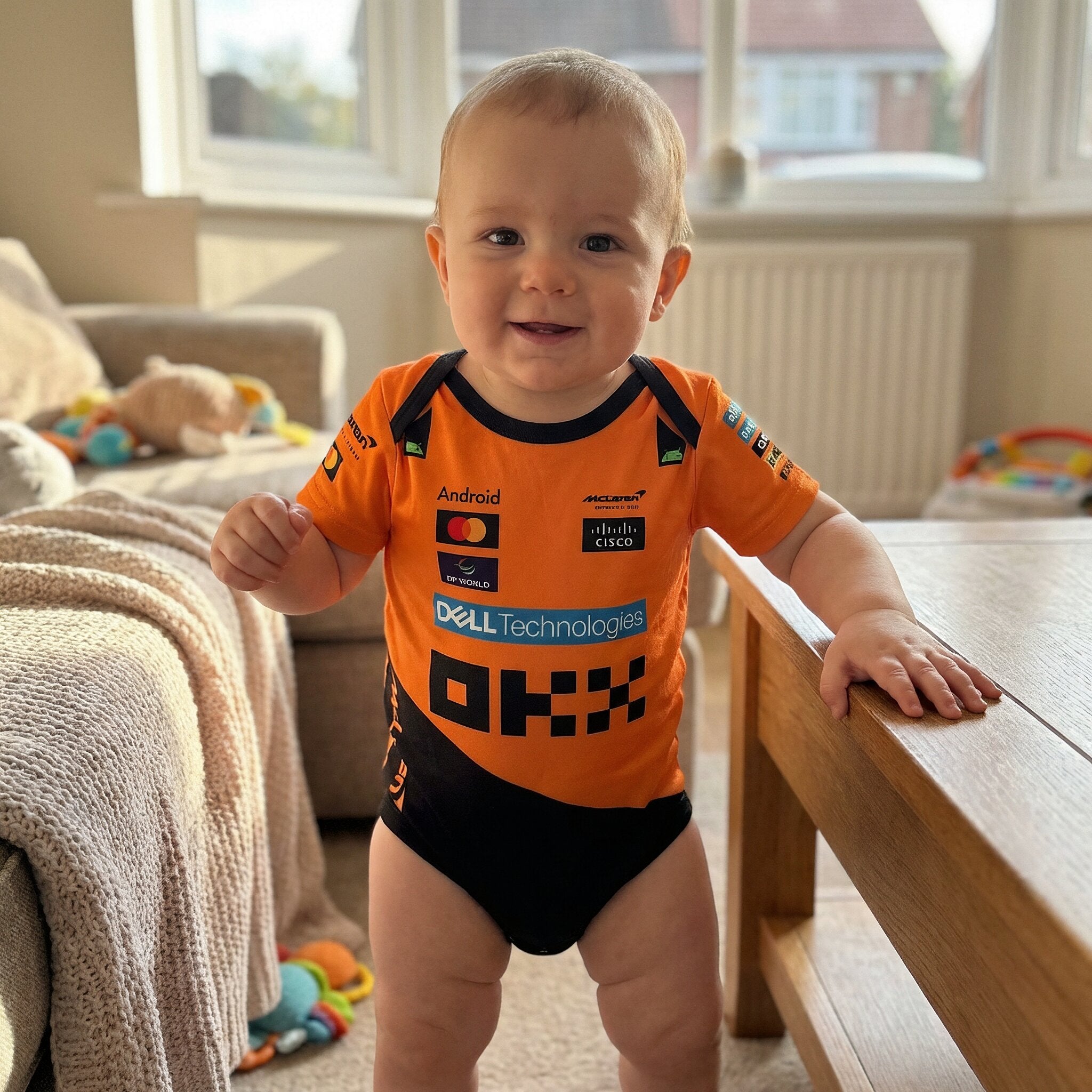 McLaren Baby Bodysuit Onesie 2025 - baby wearing a 2025 mclaren racing baby bodysuit onesie in a bright living room | Dash Racegear